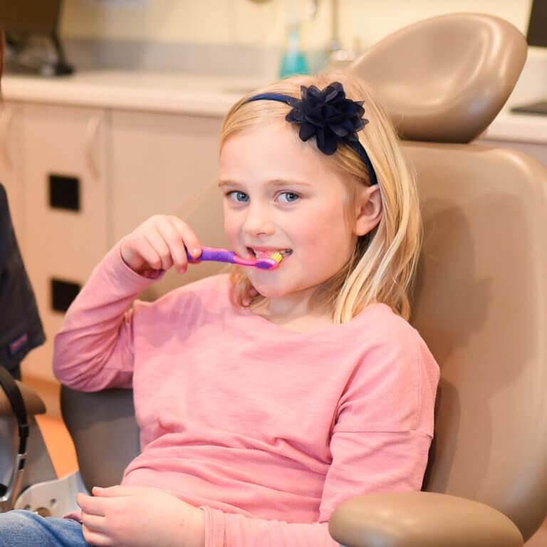 A tween girl sitting in a dentist chair brushing her teeth